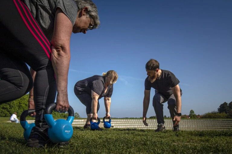 Nicolas og bootcampdeltagere i solskin i Folkeparken, roskilde, de træner med kettlebells og øver teknikker